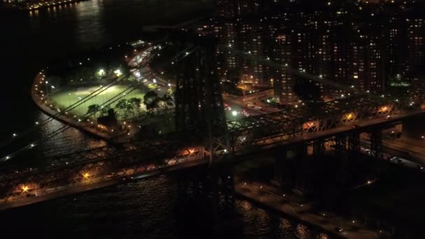 空中のヘリ ショット ニューヨーク市のマンハッタン住宅地小さなドイツ地区につながる夜ヒストリック ウィリアムズバーグ橋ライトアップ 忙しい高速道路通勤する車でいっぱい — ストック動画