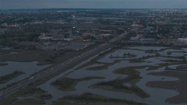 空中ヘリショット 日没後に港に向かってニュージャージー湿地の土地を通ってターンパイクハイウェイの上を飛ぶ ニューアーク湾の工業化された商業地帯の蛇行川 — ストック動画