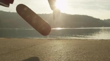 Ağır çekim, Close Up: kaykay ve altın ışık günbatımında nollie kickflip hüner okyanus boyunca kaldırımda atlama tanınmaz kaykaycı. Denizin kenarında kaykay yapan kaykaycı