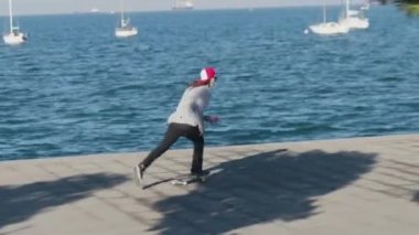 Yakın: kaykay ve gemi port yakınındaki Bulvarı'nda güneşli yaz gününde yürüyüş yayalar geçmiş beton okyanus kıyısında sürme kickflip hüner atlama Pro kaykaycı