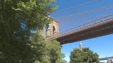 Ağır çekim, düşük görüş açısı, Close Up: Tarihi Brooklyn Bridge çevrili yemyeşil yeşil ağaç Kanopiler karşı çarpıcı mimari tasarımının ayrıntılarını temizleyin mavi gökyüzü güneşli günde New York'ta