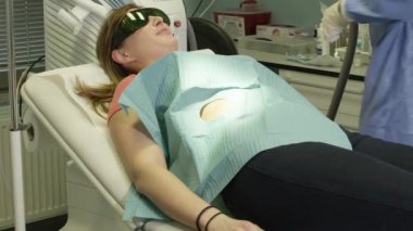 Yakın plan: genç bayan hasta özel dermatolojik estetik cilt merkezinde lazer köstebek temizleme işlemi yaptırıyor. Doktor dermatolog doğum lekesini lazerle buharlaştırarak temizliyor.