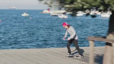 Yakın: kaykay ve ollie atlama genç kaykaycı flip hüner beton oceanfront sıcak güneşli yaz gününde sokak üzerinde. Kaykaycı çocuk Kickflip hile deniz kenarında kaykay ile atlama