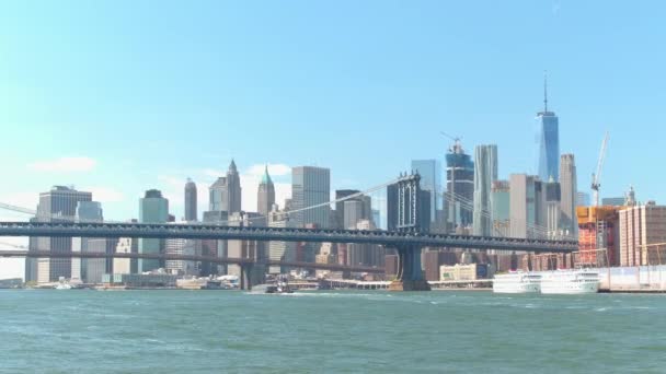 イースト リバーにマンハッタンとブルックリン橋の視点からバック グラウンドでダウンタウンのニューヨーク マンハッタンのスカイラインの象徴的なビュー に対して有名な現代ガラス高層建築の澄んだ青い空 — ストック動画