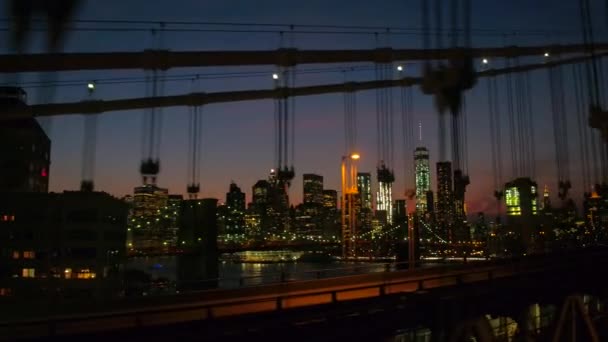 夜ダウンタウンのビジネス地区に街の明かりで照らされたの建物を象徴的なブルックリン ブリッジとモダンなガラスの高層ビルと高層を見渡す有名なマンハッタン橋を運転 — ストック動画