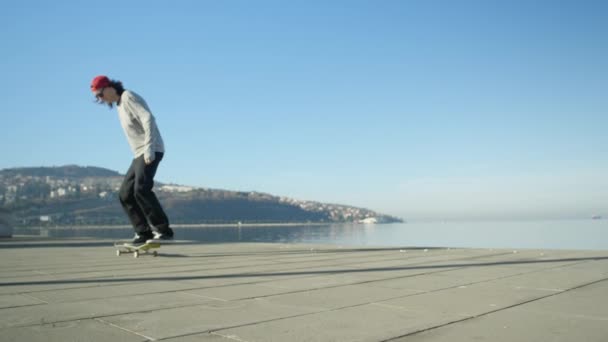 关闭慢动作 年轻的专业滑板滑板和跳跃奥利在海滨漫步在阳光明媚的夏天的小伎俩 滑板跳跃 Kickflip 魔术与滑板附近的海洋 — 图库视频影像