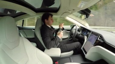 Yakın: özerk kendi kendine sürüş otomatik pilot lüks elektrik sürücüsüz arabada seyahat ederken direksiyonuna alkol sorumsuz genç iş adamı. Erkek sürücü sürüş sırasında votka içiyor