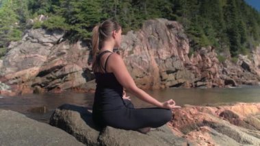 Close Up: Kırmızı volkanik kayalık sahilde oturan ve rahatlatıcı güneşli bahar günü zevk çekici genç kadın meditasyon. Kız yemyeşil büyümüş vahşi doğada deniz kıyısında meditasyon yaparken rahatlatıcı