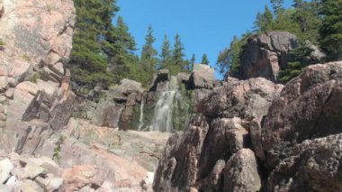 Yakın: rocky yosunlu uçurumun kırmızı volkanik taşlı Cape Breton Adası'nda düşen kristal berraklığında dağ bahar. Cliffy engebeli gür yeşil ağaçlarıyla kaplı