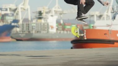 Ağır çekim yakın çekim: kaykay ve beton okyanus kıyısında güneşli günde arka seaport limanında demirlemiş yük gemisi gemi sürme heelflip hüner atlama Pro kaykaycı