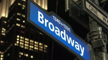 Close Up, Dof: Ünlü mavi renkli Broadway sokak işareti gece yanan pencereler ile ikonik Empire State Binası üzerinde bir kutup üzerinde. Işıklı ofisleri ve üst aydınlatma ile modern camgökdelen