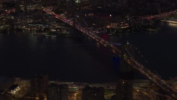空中ヘリ ショット 表示商標 自動車交通が象徴的なブルックリン橋を渡って動くライトアップ灯不思議な夏の夜にニューヨーク市で 忙しい高速道路や路上で密な交通 — ストック動画