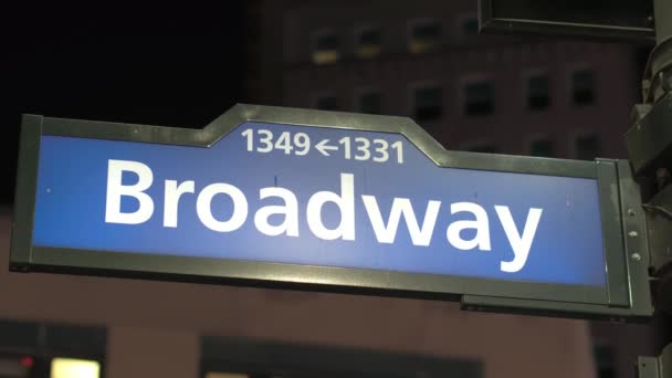 近距离 Dof 著名的蓝色百老汇交通标志路标上街角的曼哈顿 纽约市在夜间 高层住宅塔座与低层公寓楼背景 — 图库视频影像