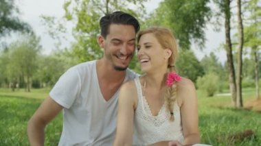 Ağır çekim, Close Up, Dof: güzel sarışın beyaz bir kadın ve yerel park yere oturuyor ve işaret parmağınızla şeklinde kalp yapma koyu saçlı adam. Mükemmel bir çift aşık güneşli gün zevk