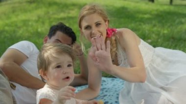 Ağır çekim, Close Up, Dof: mükemmel aile piknik park güneşli yaz gününde. Mutlu baba ve anne yalan battaniye, neşeli kızı beslenme bebek bisküvi, yalama ve çalmak şirin küçük köpek