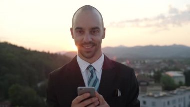 Ağır çekim, Close Up, Dof: açık havada çalışan yazma iletileri ve e-posta yolu ile cep telefonu ayakta şehrin yukarısındaki çatıda şaşırtıcı Altın ışık günbatımında göndermek başarılı mutlu işadamı