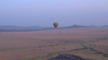 Hava: yüksek güzel mor hafif puslu sabah yere uzak ova düzlüklerinde yukarıda gökyüzünde yüzen Safari sıcak hava balonu. Şaşırtıcı Afrika vahşi doğada şafakta balon turist