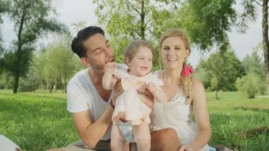 Ağır çekim, Close Up, Dof: onu yukarı ve aşağı çarpıcı güneşli günde savurma kucağında, neşeli bebek kız ile oynarken mutlu genç baba. Yanı sıra paket üzerinde oturan ve gülümseyen güzel neşeli anne