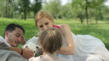 Yakın kadar ağır çekim Dof: Parkta piknik köpek mükemmel bir aile. Mutlu baba köpek, neşeli bebek kızı ve güzel karısı gün zevk onun yanında oturan sevişme battaniye yatan