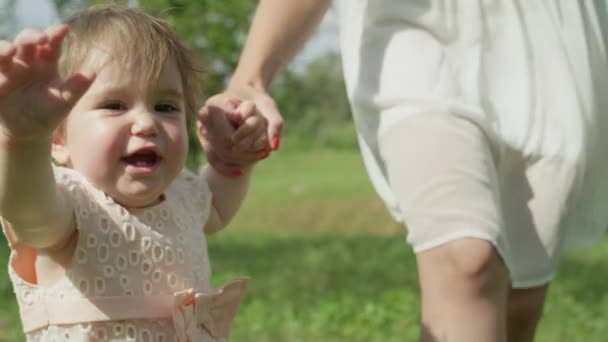 慢动作 自由度 可爱的小女孩牵着手与年轻的母亲和在当地公园的第一步 在完美的阳光明媚的夏日 开朗高兴的女儿在大自然中的乐趣 — 图库视频影像
