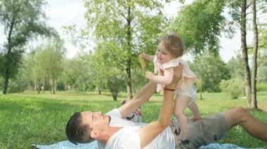 Dof kadar yavaş hareket yakın: genç baba yerel Park, yerde yatan küçük uçak oynayan neşeli tatlı bebek kız ile gülümseyen. Eğleniyor havada süzülerek pembe elbiseli gülümseyen kızı