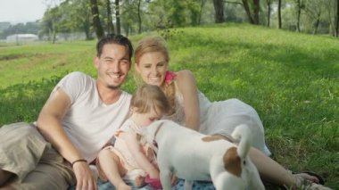 Ağır çekim, Close Up, Dof: parkta kaliteli zaman geçirmek mükemmel genç bir aile. Bisküvi, köpek onları çalmak tatlı yeme gülümseyen kız bebek. Güzel anne ve neşeli baba izliyor ve gülüyor