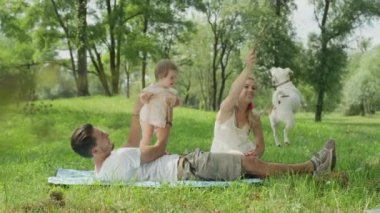 Ağır çekim Dof yakından: Oldukça genç eş ve bebek kızıyla birlikte üzerinde park battaniyeye oturmuş ve onu bir sopayla alay Jack Russell köpekle oynayan kadın. Kalite aile zaman doğada