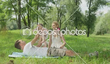 Ağır çekim, Close Up, Dof: mumya ve battaniye var yalan, şirin bebek kızı elinde tutan ve güzel güneşli yaz günü uçak yerel parkta oynarken mutlu genç baba gülümseyen güzel sarışın