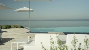 Ağır çekim, Close Up: boş otel beach süslü beyaz daybeds, şezlong ve şemsiye pahalı lüks tatil güneşli yaz gününde çarpıcı. Sonsuza kenar havuz bakan mavi sonsuz bir okyanus