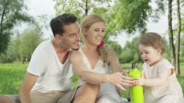 Ağır çekim, Close Up, Dof: yumuşak battaniye güzel Central Park'ta zeminde oturan sevgi dolu sevgi ailesi için şişe su veren tatlı bebek kız. Doğada neşeli mükemmel aile