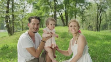 Ağır çekim Dof yakından: yaz günü mükemmel güneşli kucağına neşeli bebek kızla oynamak mutlu genç baba. Yanında oturan ve gülümseyen güzel neşeli anne. Küçük köpek kökenden döşeme