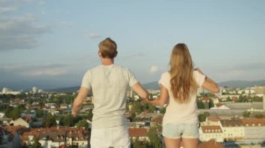 Ağır çekim kadar yakın: Heyecanlı kız ve elele ve onları yükselen güneş tarafından aydınlatılmış kentsel şehir üzerinde çatı üzerinde havada yükselterek mutlu çocuk. Başarı kutluyor ve hayat sevgi dolu mutlu insanlar