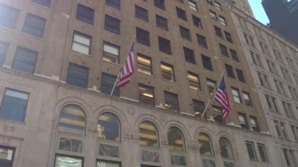 低角度のビュー クローズ アップ 近代都市景観ニューヨークの日当たりの良い夏の日に 上げられたアメリカ国旗と近所の事務所ビルを反映して大きなガラス窓と背の高い超高層ビル — ストック動画