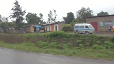 Arusha, Tanzanya - 10 Haziran 2016: Yoksulluk içinde renkli Afrika konut köy. Yerli halk tarafından motosiklet seyahat ve yağmurlu günde yürüme mesafesinde ve yağmurluklar çamurlu asphalted Road