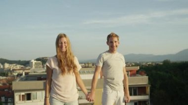 Ağır çekim kadar yakın: Heyecanlı kız ve elele ve onları üstünde yükselen güneş tarafından aydınlatılmış kentsel şehir üzerinde çatı yükseltmek boy gülümseyerek. Başarı kutluyor ve hayat sevgi dolu mutlu insanlar