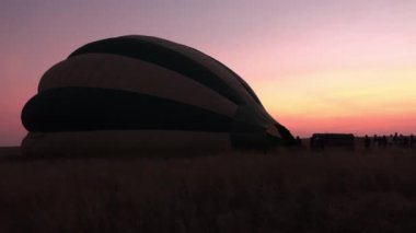 Yakın: Serengeti çarpıcı Balonculuk macera hazırlıkları. Açık kısa otların savannah sahada sabah pembe ve mor gökyüzü altında yatan renkli safari sıcak hava balon şişirme