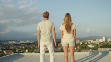 Dof kadar yavaş hareket yakın: erkek holding kız arkadaşı bakımı ve onu inanılmaz altın günbatımında bir gökdelenin tepesinde öpüyor. Mutlu genç çift romantik tarihte gündoğumu güzel kentsel şehir üzerinde üzerinde