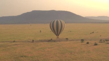 Anteni: sıcak hava balon uçan turist dolu Safari yerden kapatın. Büyülü Afrika sahnesi, savannah kısa çim alan ve altın ışık sabah çarpıcı üzerinde mesafe içinde büyümüş dağlar