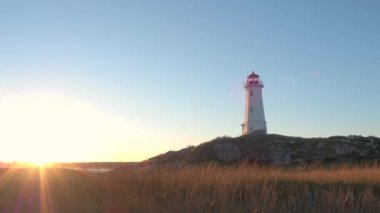 Nova Scotia Yarımadası'nın Kuzey Atlantik Okyanusu, Kanada Altın ışık batımında yukarıda yükselen kayalık ve çimenli kıyısında güzel Louisbourg feneri ayakta. Deniz kıyısı üzerinde kuru saman aydınlatıcı yapraklara