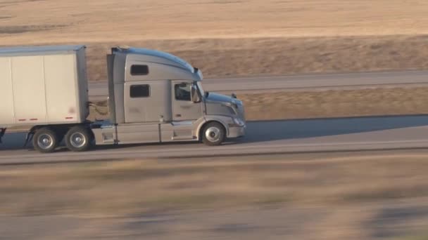 閉じるを貨物コンテナー半トラックがアメリカ グレートプレーンズの草原フィールドを空の州間高速道路に沿って運転の商品を運搬します 晴れた夜に出荷貨物をトレーラーします — ストック動画