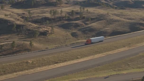 航空貨物コンテナー セミトラック日当たりの良いでこぼこ丘陵風景を介して実行している空のハイウェイに沿って運転の上を飛んでします アメリカ合衆国の高速道路の旅の間で配送コンテナーをトレーラーします — ストック動画