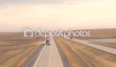Hava yakın: yük konteyner yarı kamyon eşya, arabalar, SUV'lar ve güneş doğarken ile geniş çayır alanlar vahşi Amerikan kırsal kesimde çalışan Great Plains yolu boyunca seyahat transfer çekme