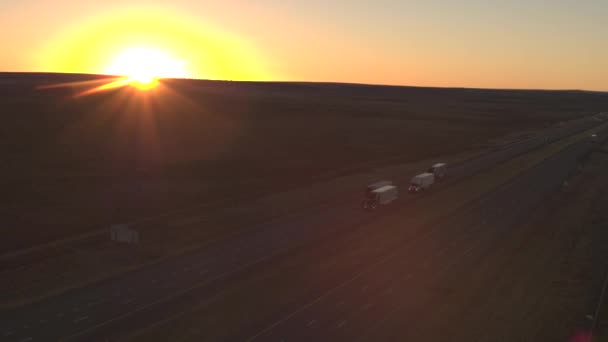 空中飞行 在美国大平原的黄昏 在繁忙的公路上行驶的货运车上装载着货物 在金色夕阳下运输和运送货物的半卡车 — 图库视频影像