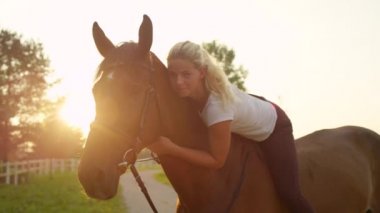 At boynu karşı başını döşeme ve onun sevgili mare kucaklayan ağır çekim yakın kadar Dof güzel sarışın kız. Genç ve güzel kadın sakin güneşli yaz sabahı iğdiş edilmiş hayvan çarpıcı bareback binicilik