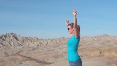 Ağır çekim: Badlands ulusal park yürüyüş ve yukarı sivri Kumtaşı Dağları güneşli günde bakan Kollarını zaferle yükselterek kadın turist. Neşeli kadın kutluyor ulaşan dağın