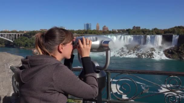 クローズアップ アメリカとブライダルベールの滝を横切ってバルコニーで見ている双眼鏡を見て女の子は岩の崖の上にクラッシュします ナイアガラ川の野生の白い滝を観察する観光客 — ストック動画