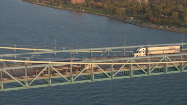 航空写真 貨物コンテナー半トラック輸送にアンバサダー橋を渡って運転 デトロイト 米国で物流センターの倉庫の上を飛んでください 複数車線の幹線道路での交通混雑 — ストック動画