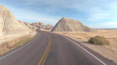 FPV: rocky Kumtaşı Dağları ile şaşırtıcı Badlands manzara geçmiş sarma boş yol boyunca sürüş. Güney Dakota'daki Badlands otlak Çölü seyahat. Yolculuk boyunca Amerika Birleşik Devletleri
