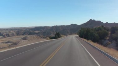 FPV: şaşırtıcı Badlands yatay, kayalık kumtaşı oluşumları ile eğri boş yol boyunca sürüş. Güney Dakota'daki Badlands Çölü seyahat. Yolculuk boyunca Amerika Birleşik Devletleri.
