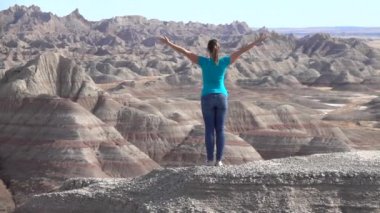 Ağır çekim: Genç kadın trekking Badlands Ulusal zevk ve rahatlatıcı güneşli gökyüzü doğru kaldırdı kollarını ile kayalık dağ tepesinde duran park. Gezgin keşfetmek Badlands vahşi